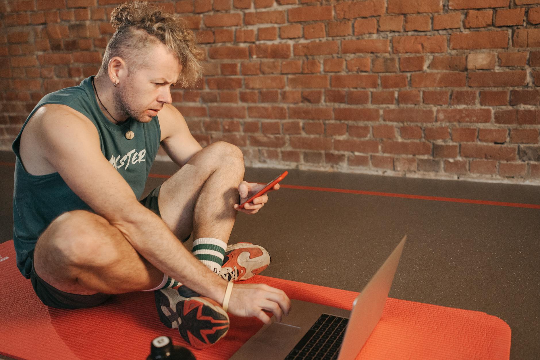 Mężczyzna siedzi na macie treningowej i planuje ćwiczenia na laptopie