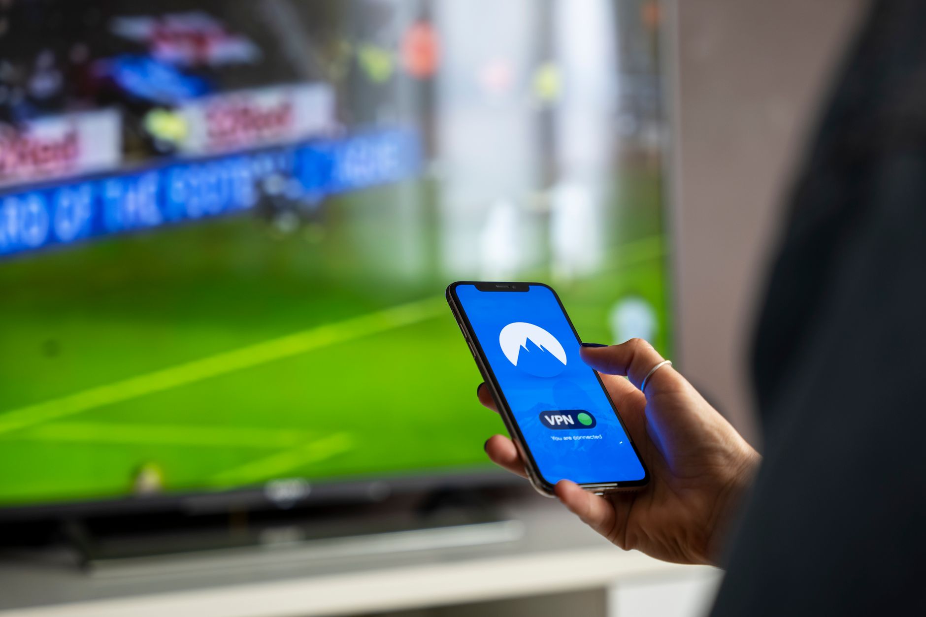Osoba z telefonem i aplikacją VPN podczas oglądania sportu na TV